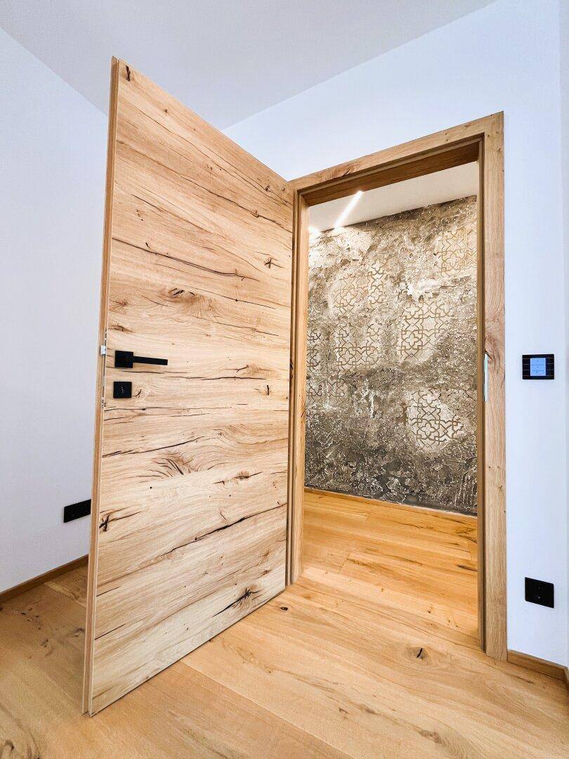 Offene Holztür mit natürlicher Maserung, die den Blick auf eine dekorierte Wand freigibt.