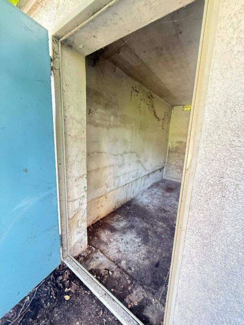 Nahaufnahme des Innenraums der Abstellkammer mit rauen Betonwänden und unebenem, verschmutztem Boden.