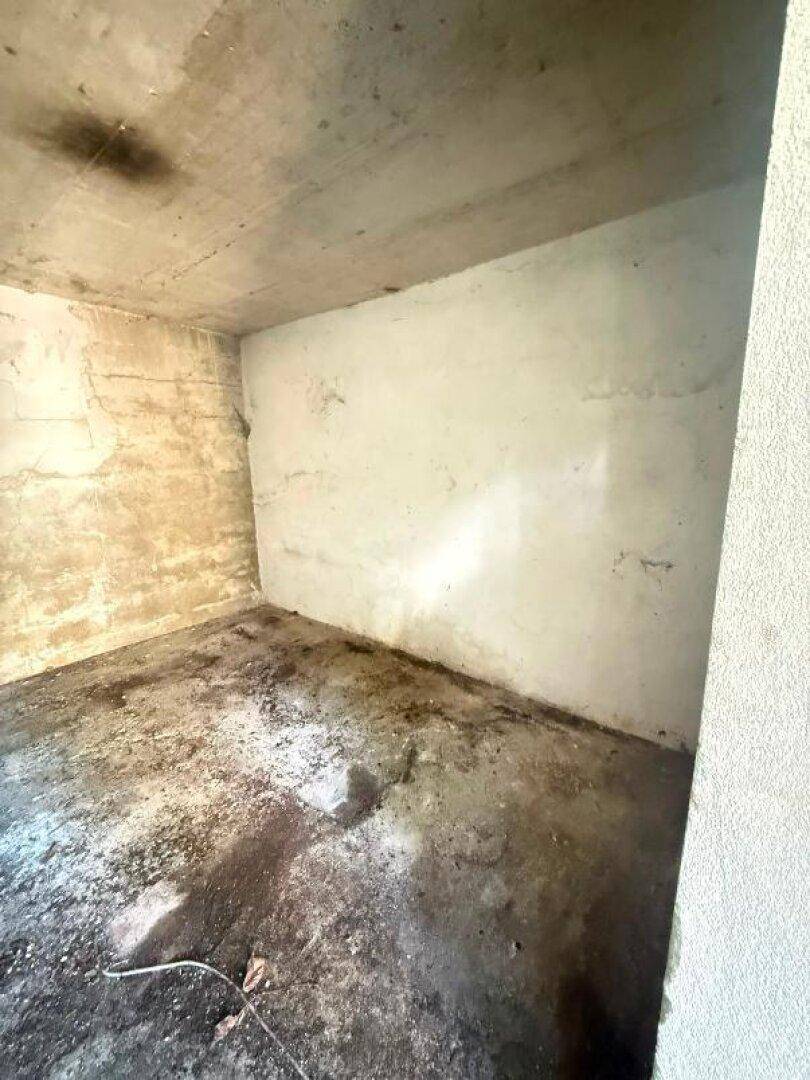 Innenansicht der Abstellkammer mit schlichten Betonwänden und einem stark verschmutzten, unebenen Boden.