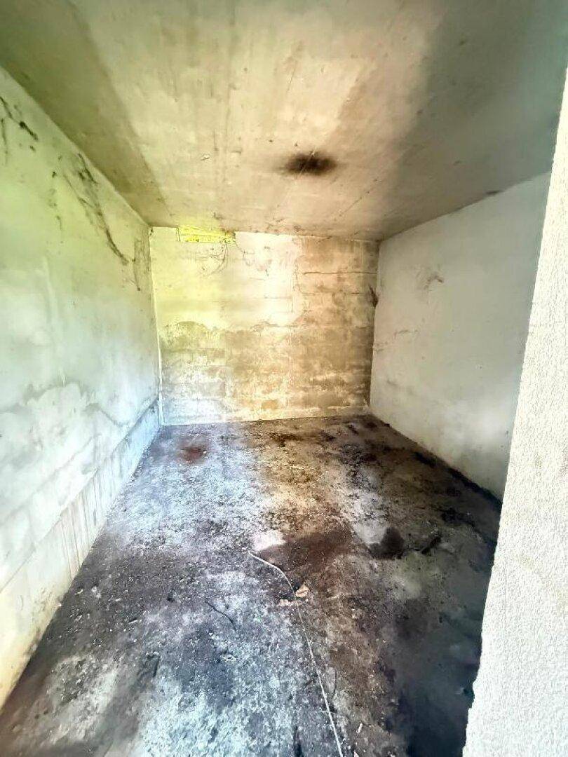 Tieferer Blick in die Abstellkammer, die rohe Betonwände und einen dunklen, unsauberen Boden aufweist.