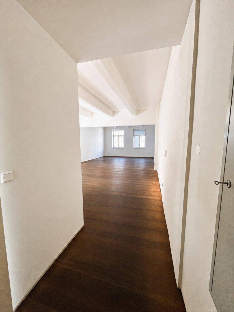Langer Flur mit Holzboden, der in einen hellen, geräumigen Bereich mit hohen Decken führt.