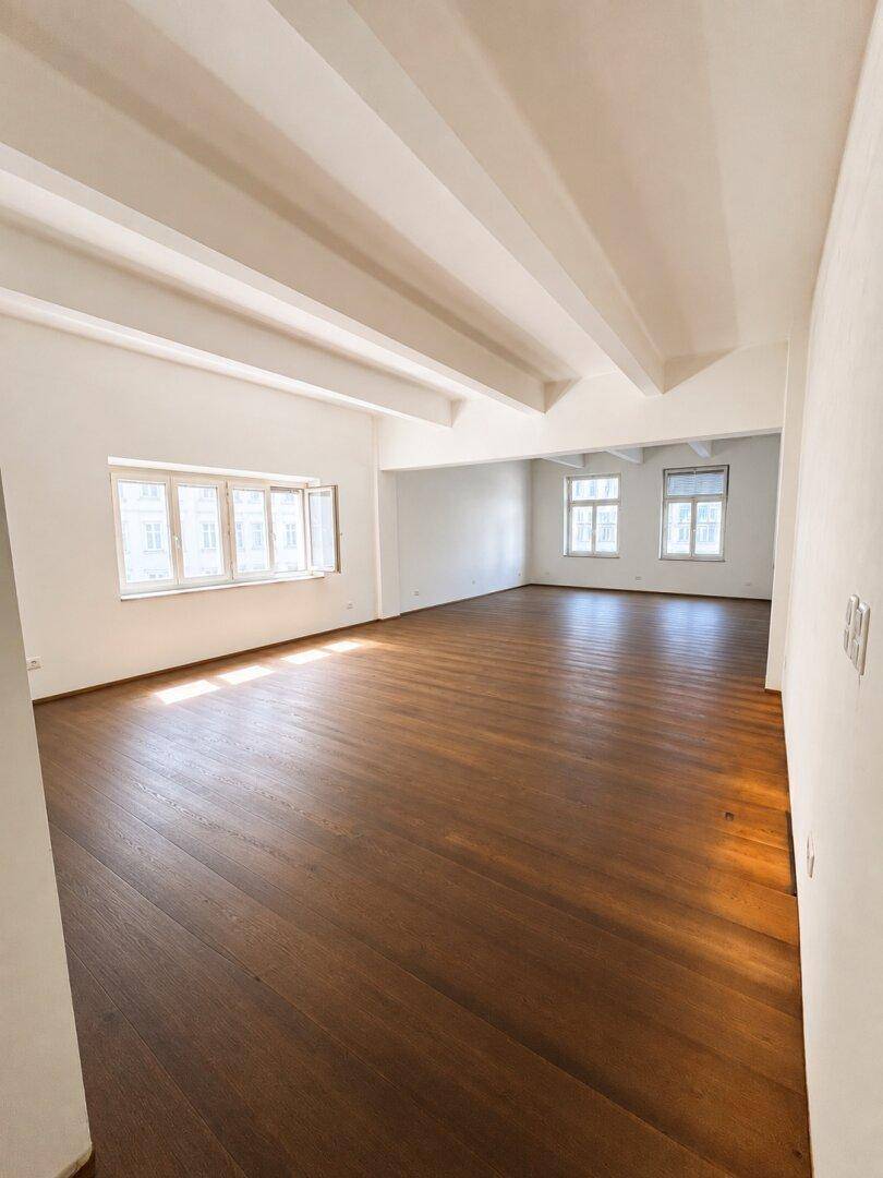 Heller, weitläufiger Raum mit dunklem Holzparkett und markanten Deckenbalken, bietet vielseitige Gestaltungsmöglichkeiten.
