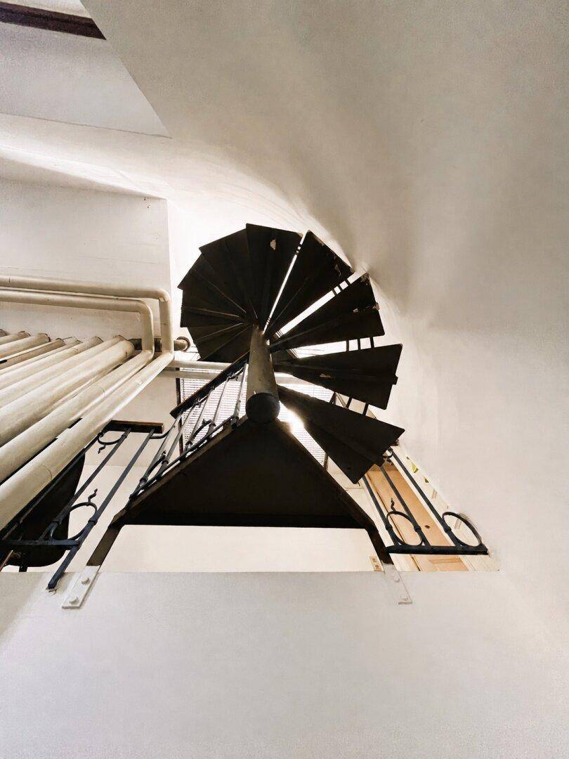 Blick nach oben auf eine schwarze Wendeltreppe aus Metall, die sich elegant nach oben windet.