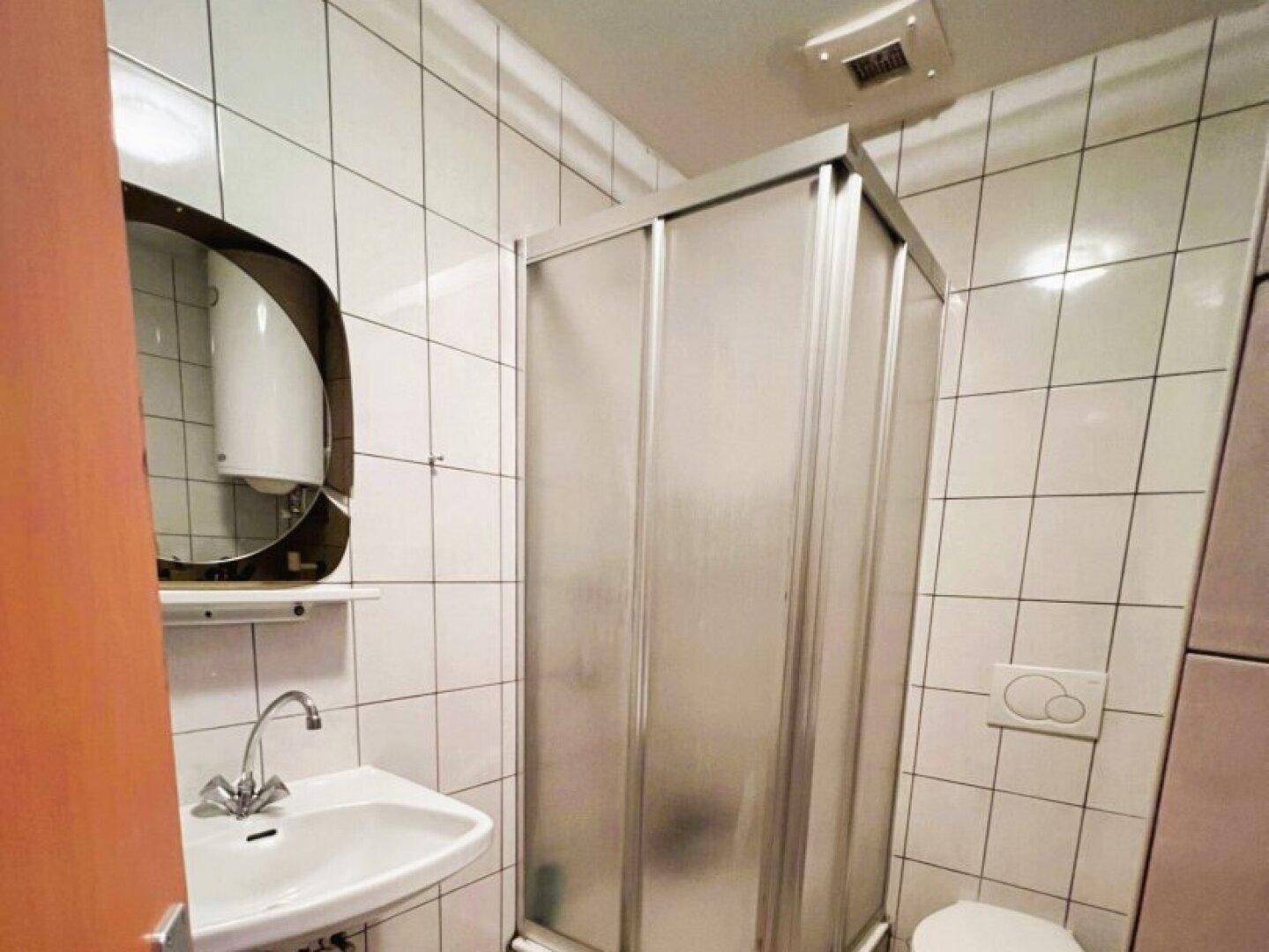 Badezimmer mit weißen Fliesen, Duschkabine, Waschbecken und Toilette.
