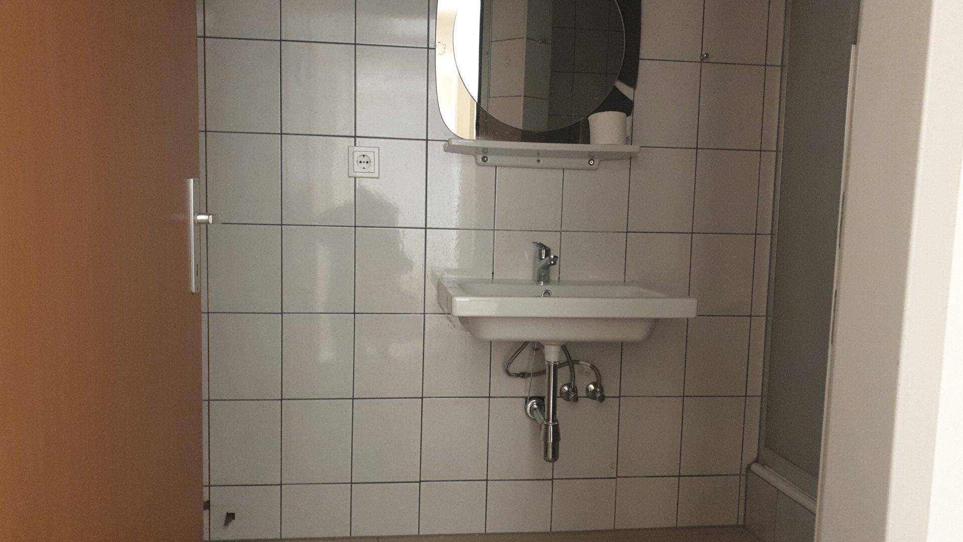 Badezimmerbereich mit weiß gefliesten Wänden, Waschbecken und Spiegel.