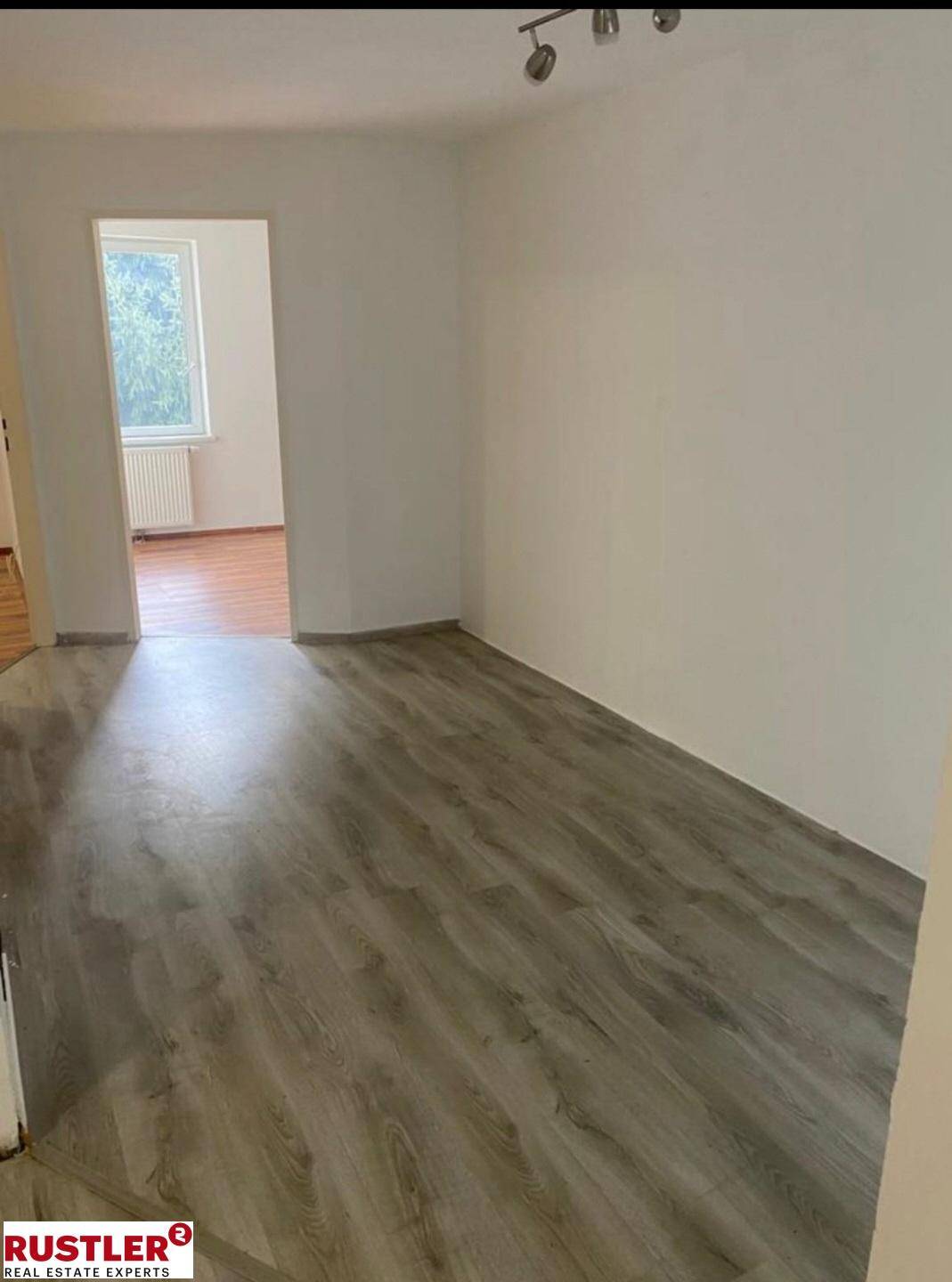 Leeres Zimmer mit hellem Laminatboden und Zugang zu einem weiteren Raum.