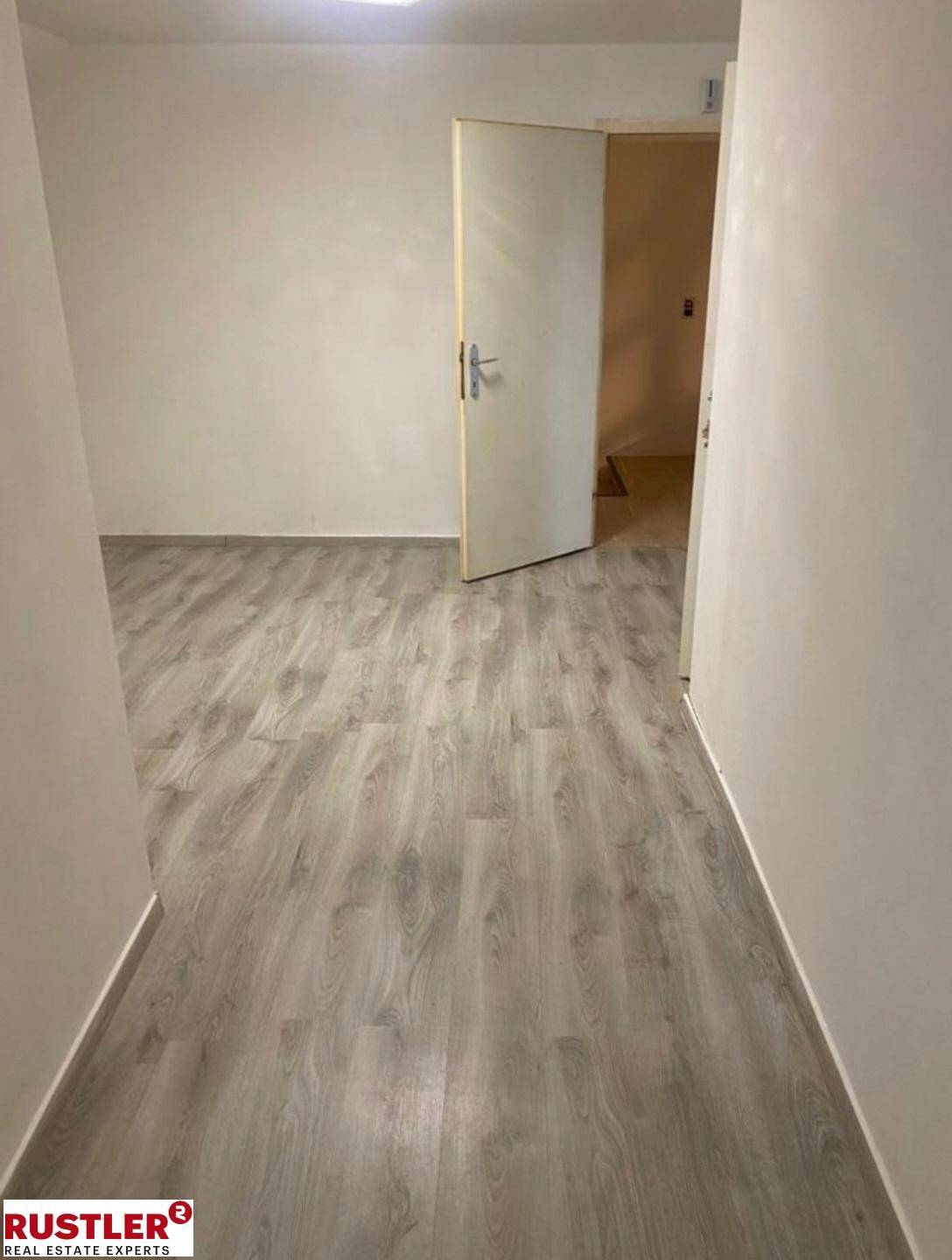 Leeres Zimmer mit hellem Laminatboden und weiß gestrichenen Wänden.