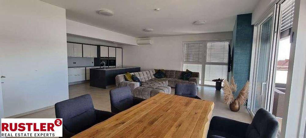 Geräumiger offener Wohn-Essbereich mit bequemer Couch, Holztisch und integrierter Küche im Hintergrund.