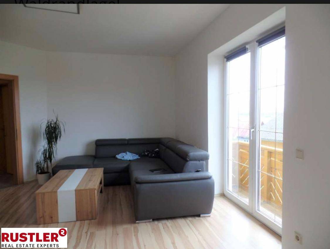 Gemütliches Wohnzimmer mit Ecksofa, Holztisch und Zugang zum Balkon.