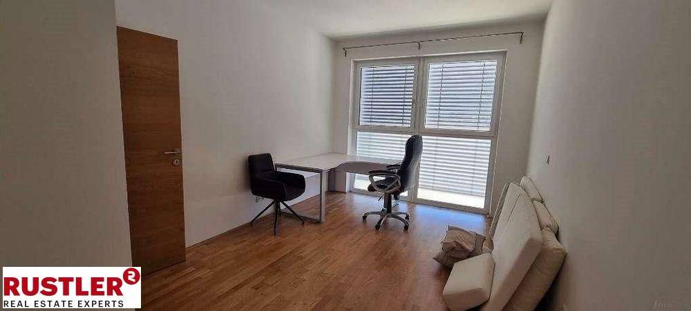 Helles Arbeitszimmer mit Holzfußboden, großem Fenster und modernem Schreibtischbereich.
