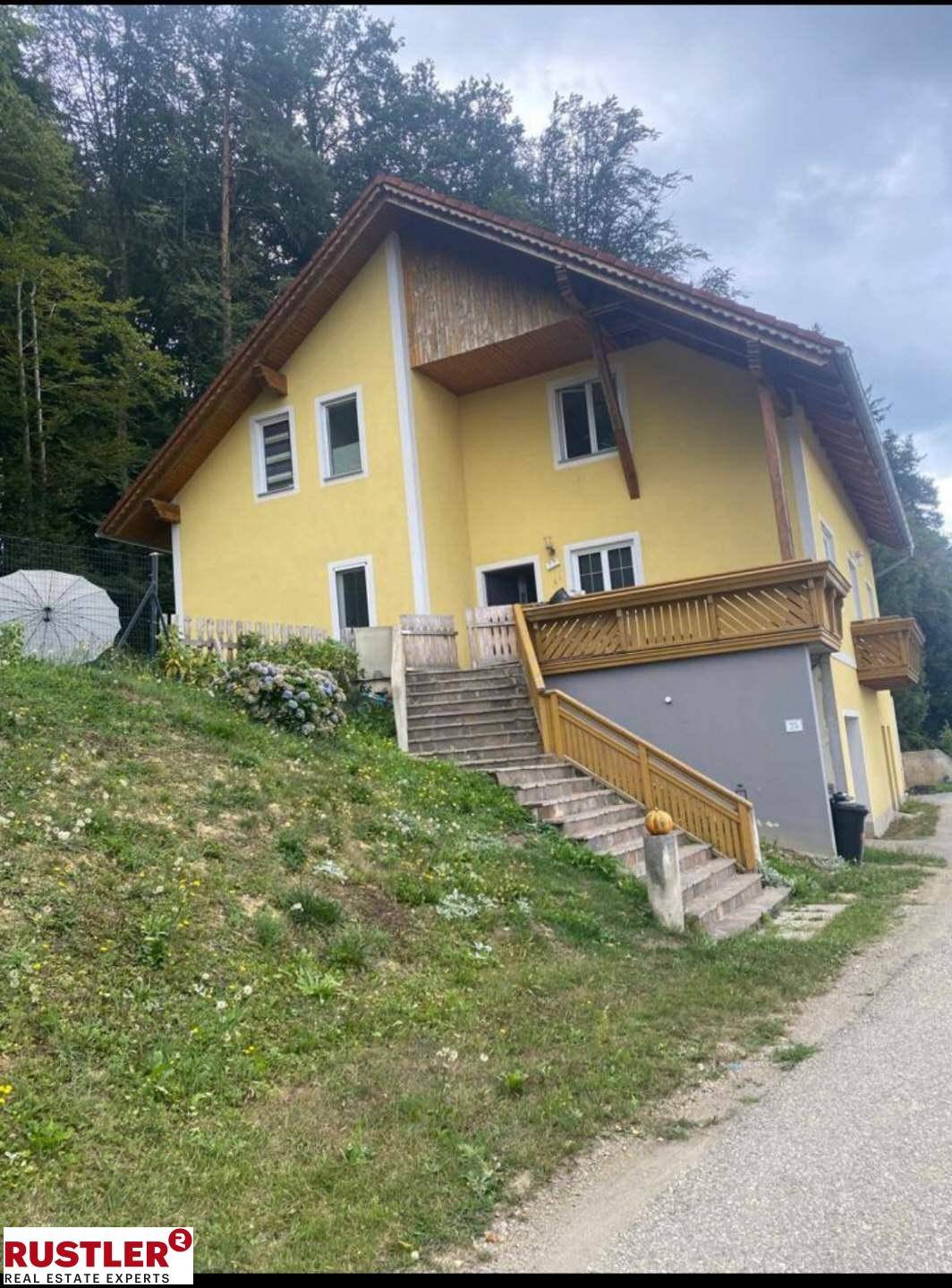 Gelbes Haus am Hang mit Außentreppe und Holzbalkon, umgeben von Natur.