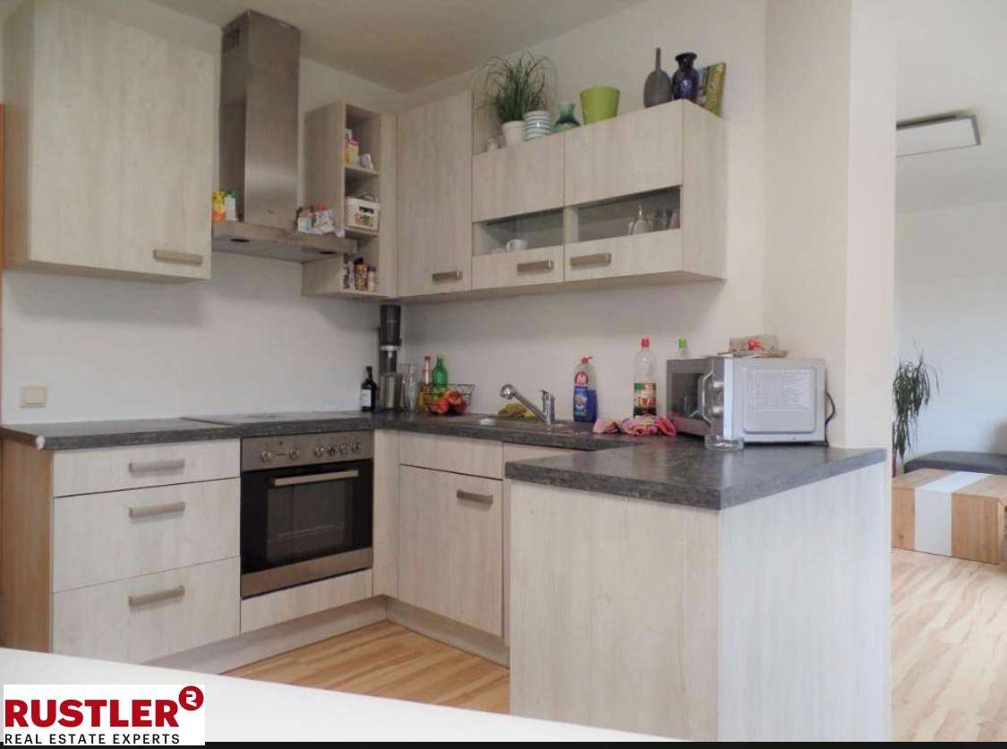 Funktionale Küche mit hellen Holzfronten, dunkler Arbeitsplatte und Edelstahlofen.