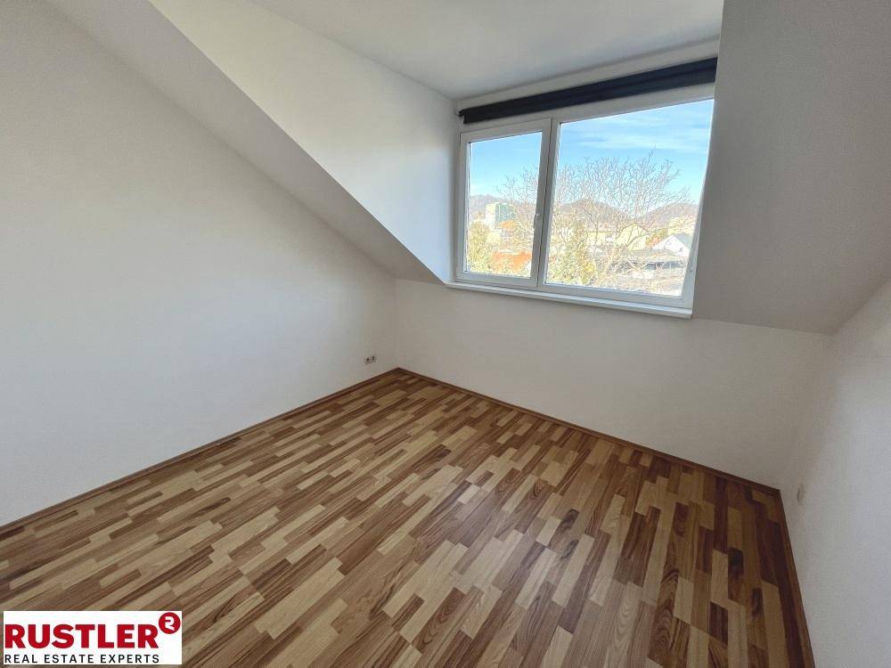 Leeres Zimmer im Dachgeschoss mit Laminatboden und großem Fenster.