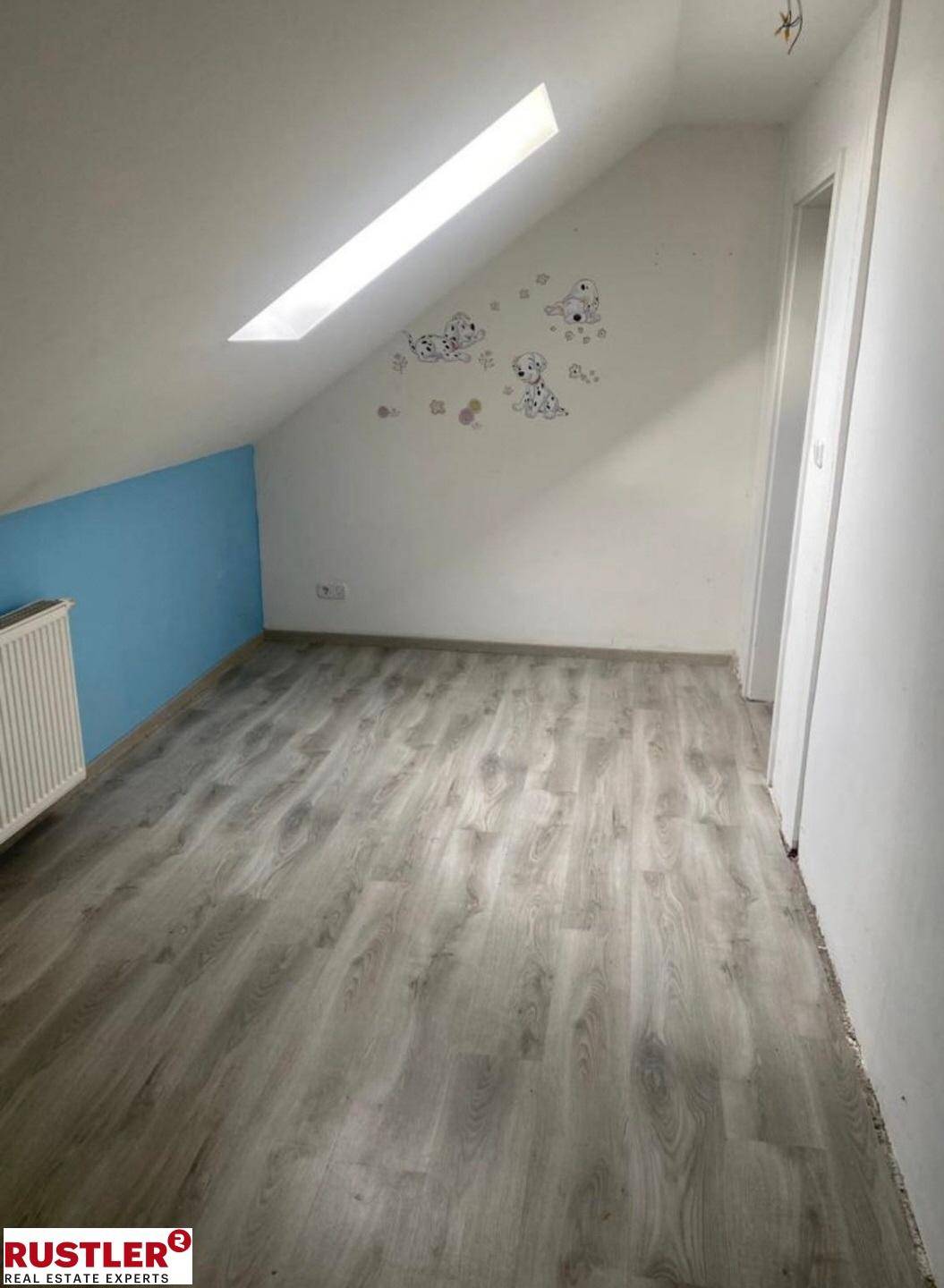 Helles Dachgeschosszimmer mit schräger Decke, Dachfenster und Laminatboden.