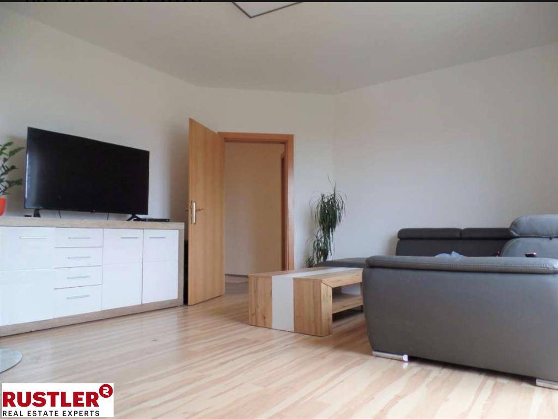Wohnzimmer mit Sofa, Fernseher auf Sideboard und Holzboden.