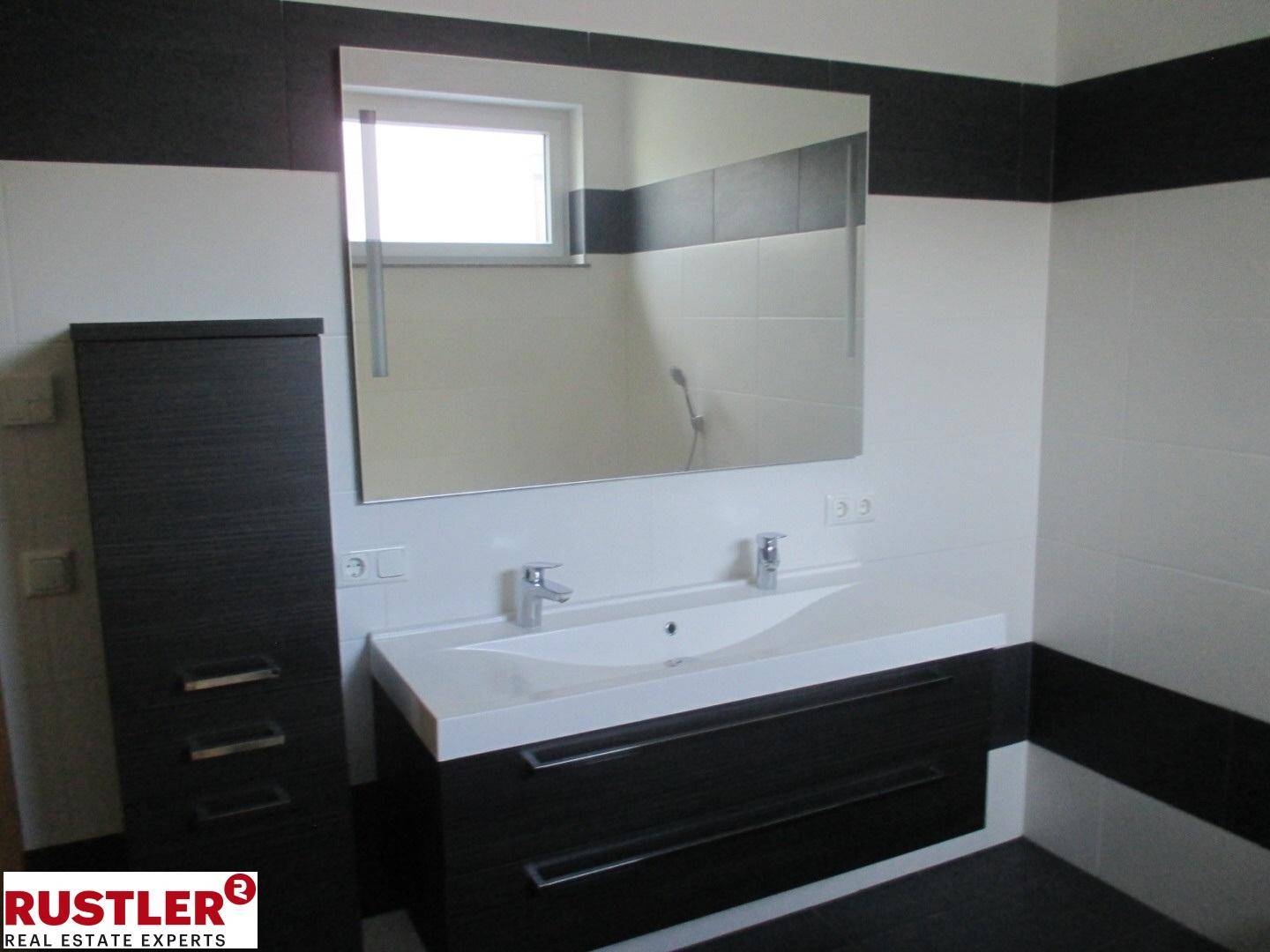 Modernes Badezimmer mit Doppelwaschbecken, großem Spiegel und schwarz-weißen Fliesen.