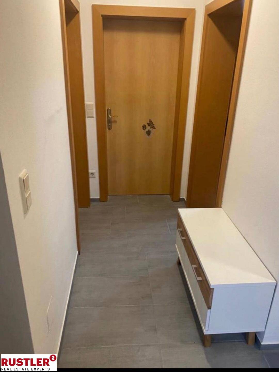 Heller Flur mit Fliesenboden und kleiner Sitzbank am Eingangsbereich.