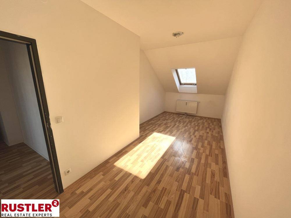 Helles Zimmer im Dachgeschoss mit Laminatboden, Dachfenster und Sonneneinfall.