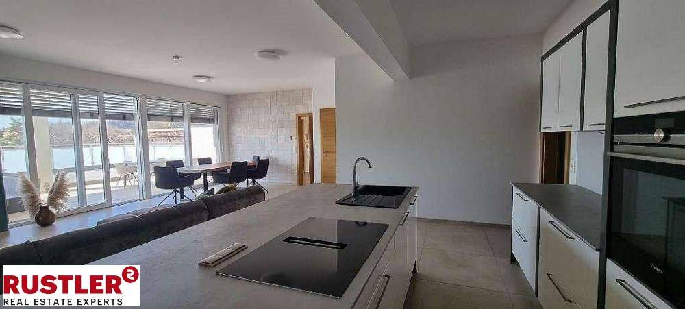 Offene, moderne Küche mit Kochinsel, integrierten Geräten und Blick auf den Wohn-Essbereich.