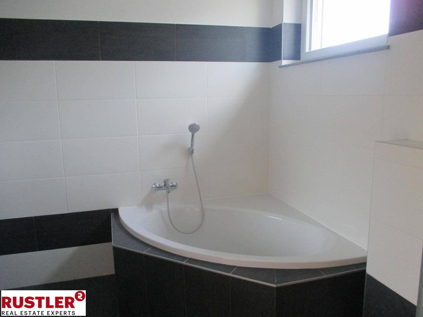 Badezimmer mit Eckbadewanne und Duscharmatur, umgeben von modernen schwarz-weißen Fliesen.