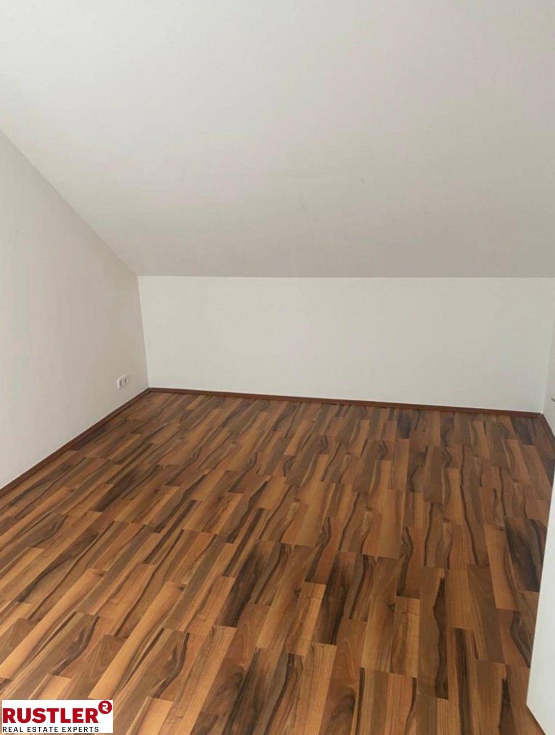 Leeres Dachgeschosszimmer mit dunklem Laminatboden und schräger Decke.