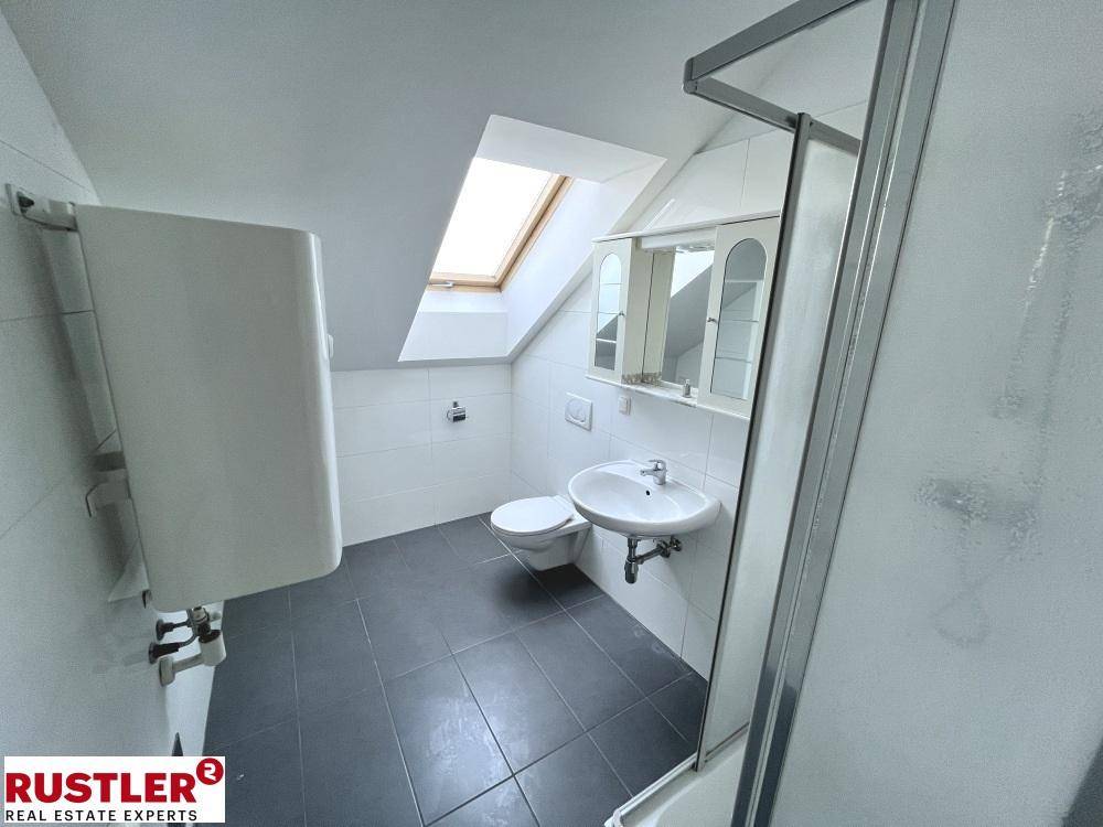 Modernes Badezimmer im Dachgeschoss mit Dusche, WC, Waschbecken und Dachfenster.