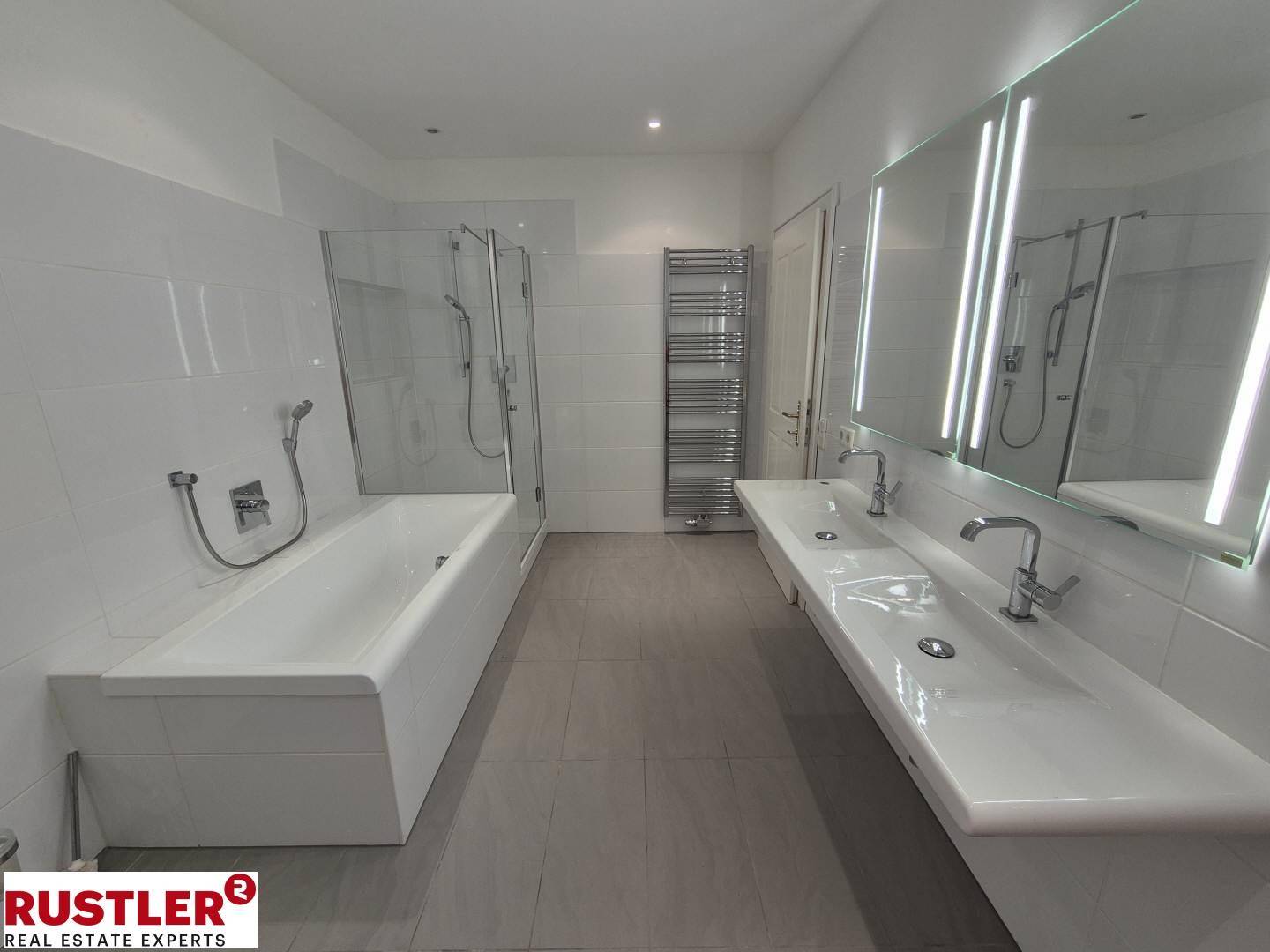 Modernes Badezimmer mit Doppelwaschbecken, Badewanne, Duschbereich und beheiztem Handtuchhalter.