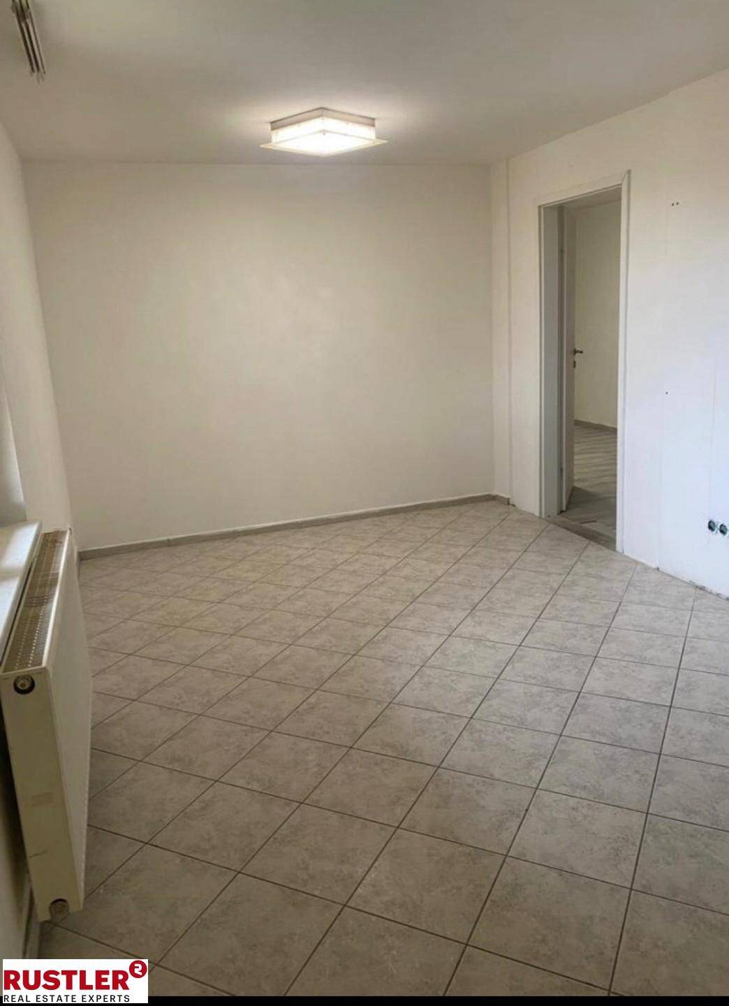 Leerer Raum mit hellen Fliesen und Heizkörper an der Wand.