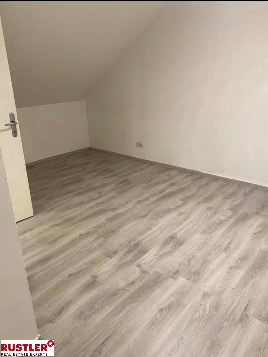 Leeres Zimmer im Dachgeschoss mit schräger Decke und Laminatboden.