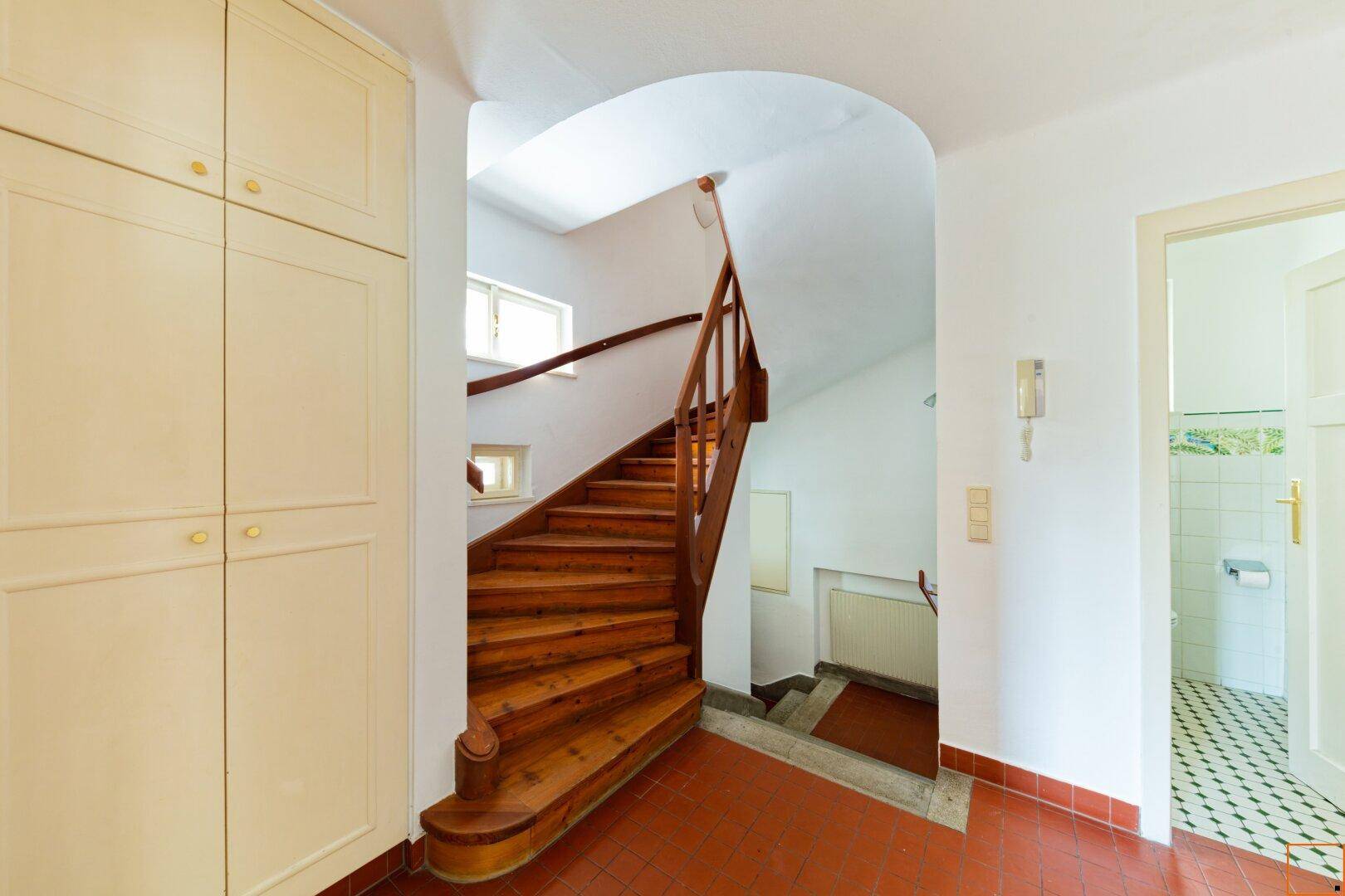 Eingangsbereich mit eleganter Holztreppe, Einbauschränken und gemustertem Fliesenboden.
