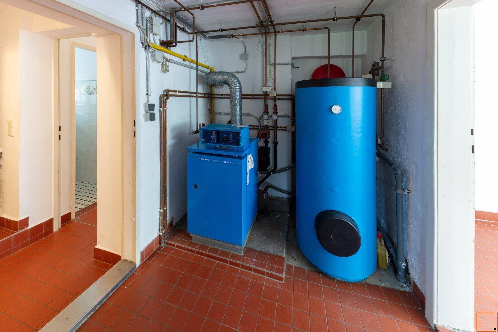Heizungsraum mit modernem Heizkessel, Warmwasserspeicher und sichtbaren Rohrleitungen.