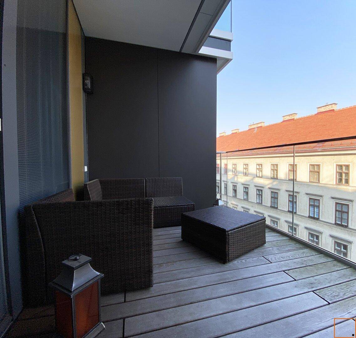 Gemütlicher Balkon mit Rattanmöbeln und Blick auf die umliegenden Gebäude der Stadt.