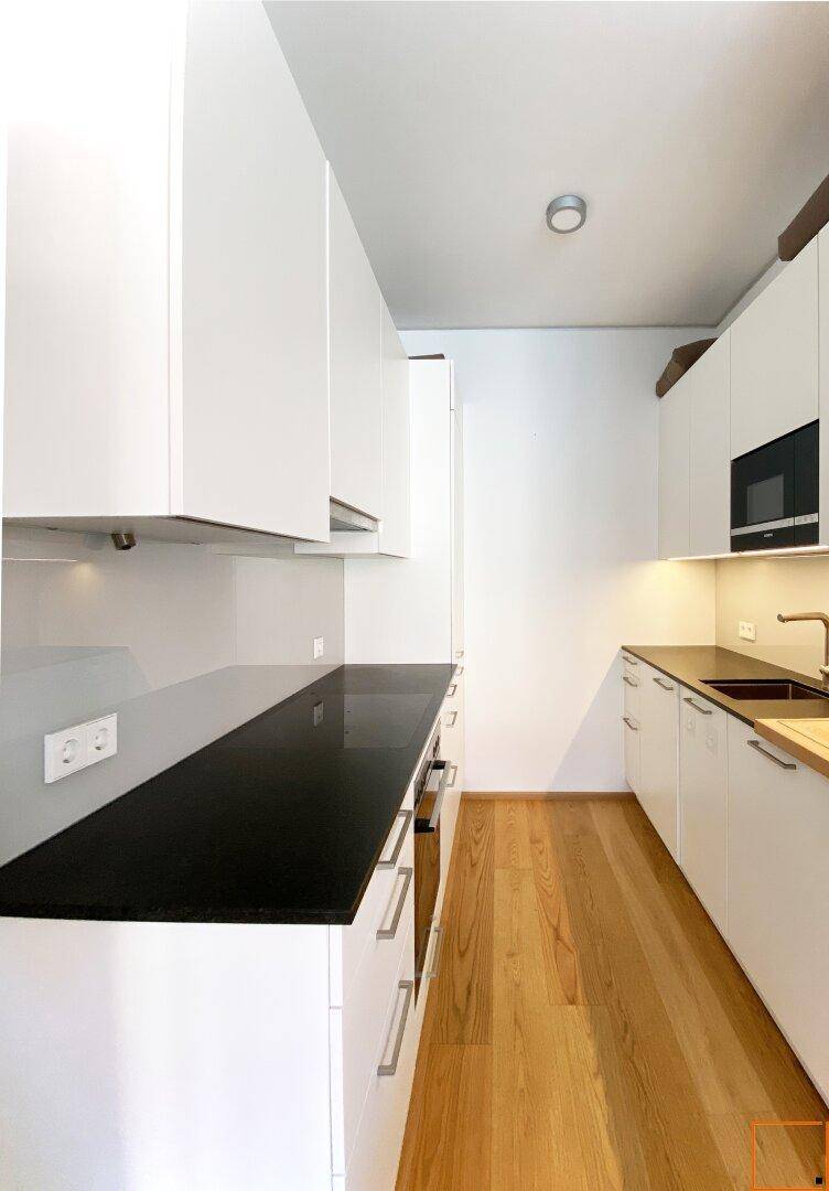 Moderne Küche mit weißen Schränken, schwarzen Arbeitsplatten und Holzboden.