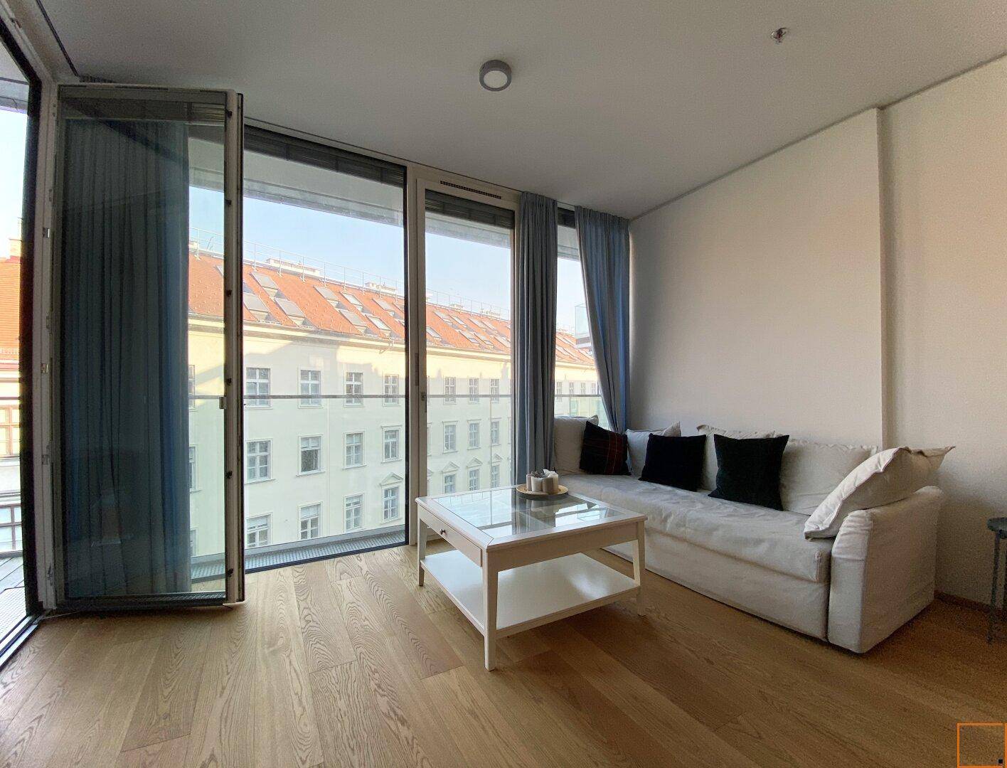 Helles Wohnzimmer mit Sofa, Couchtisch und bodentiefen Fenstern.