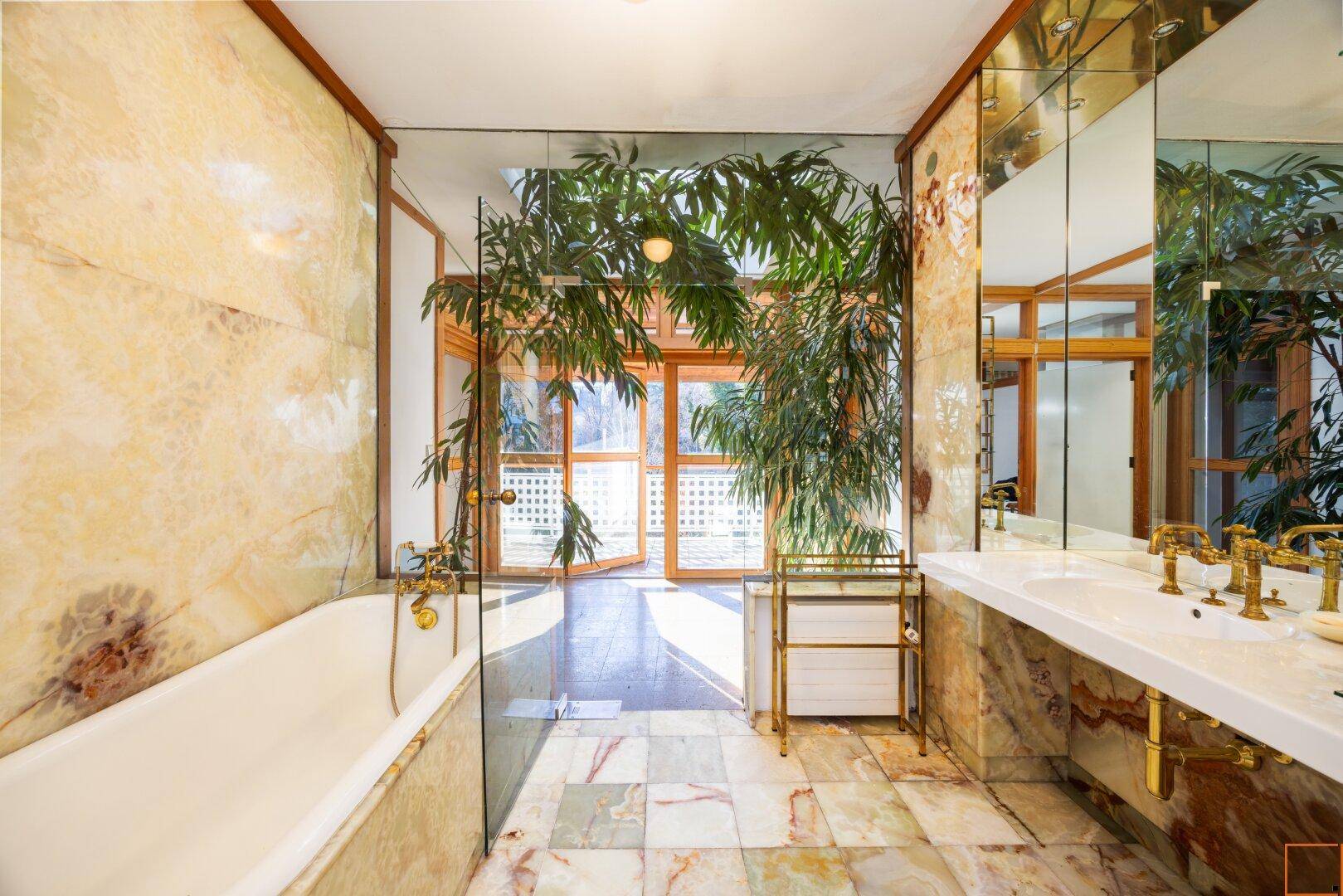 Luxuriöses Badezimmer mit doppelten Waschbecken, Marmoroberflächen und einer Badewanne, umgeben von Pflanzen.