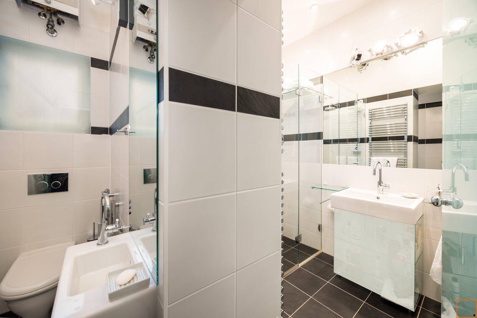 Modernes Badezimmer mit weißen und schwarzen Fliesen, einer Dusche und einem einzelnen Waschbecken.