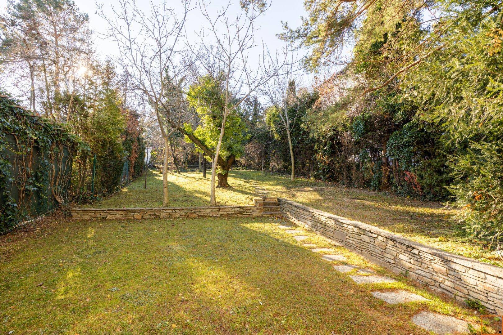 Gepflegter Garten mit einer niedrigen Steinmauer, Rasenfläche und einem Pfad.