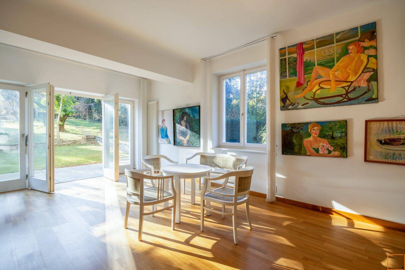 Heller Raum mit Holzboden, Gartenzugang und mehreren Kunstwerken an den Wänden.
