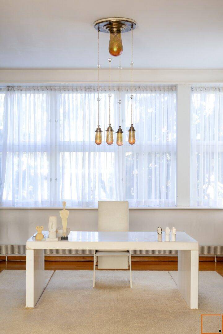 Helles Arbeitszimmer mit weißem Schreibtisch und großen Fenstern, die viel Tageslicht hereinlassen.