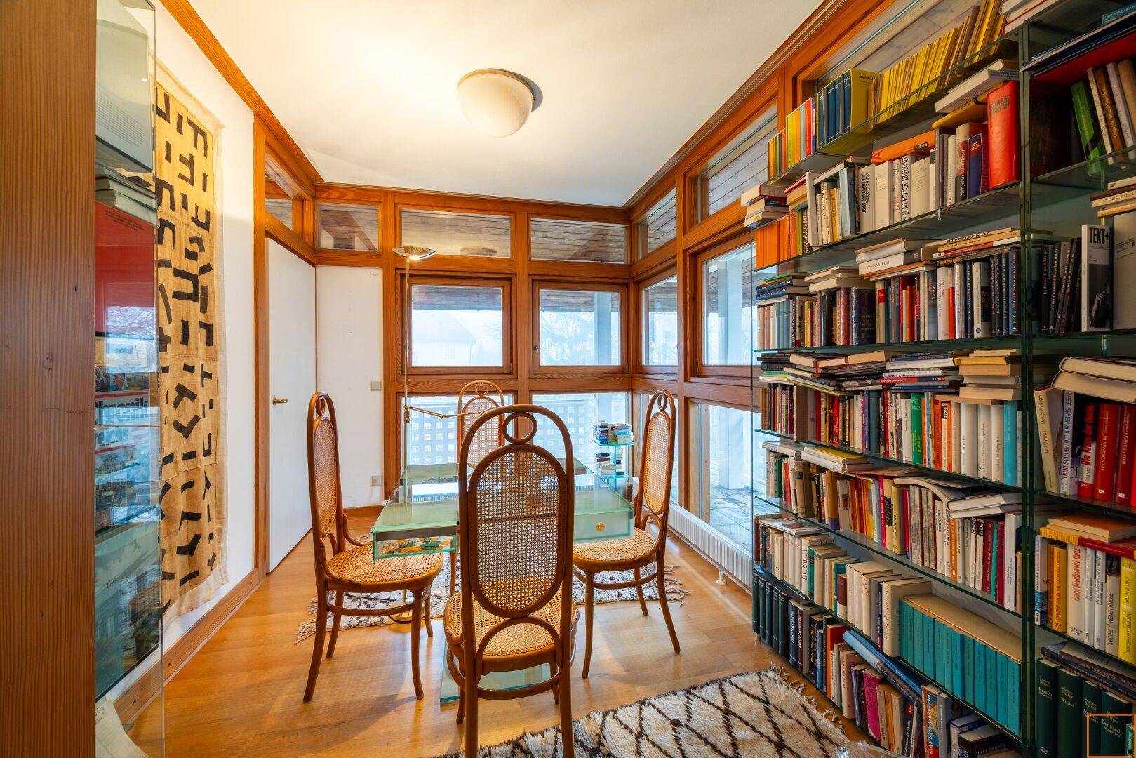 Arbeitszimmer mit Holzboden, vielen Fenstern und raumhohen Bücherregalen, die eine inspirierende Atmosphäre schaffen.