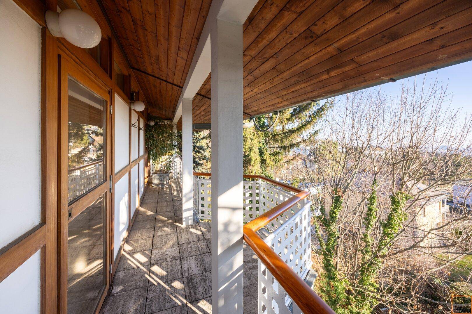 Sonniger Balkon mit Holzdecke und weitem Ausblick auf die umliegende Natur und Häuser.