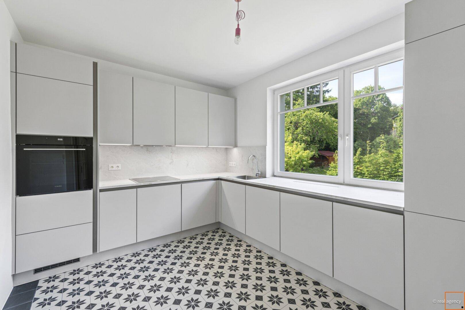 Moderne Einbauküche mit hellgrauen Fronten, integrierten Geräten und Fenster mit Grünblick.