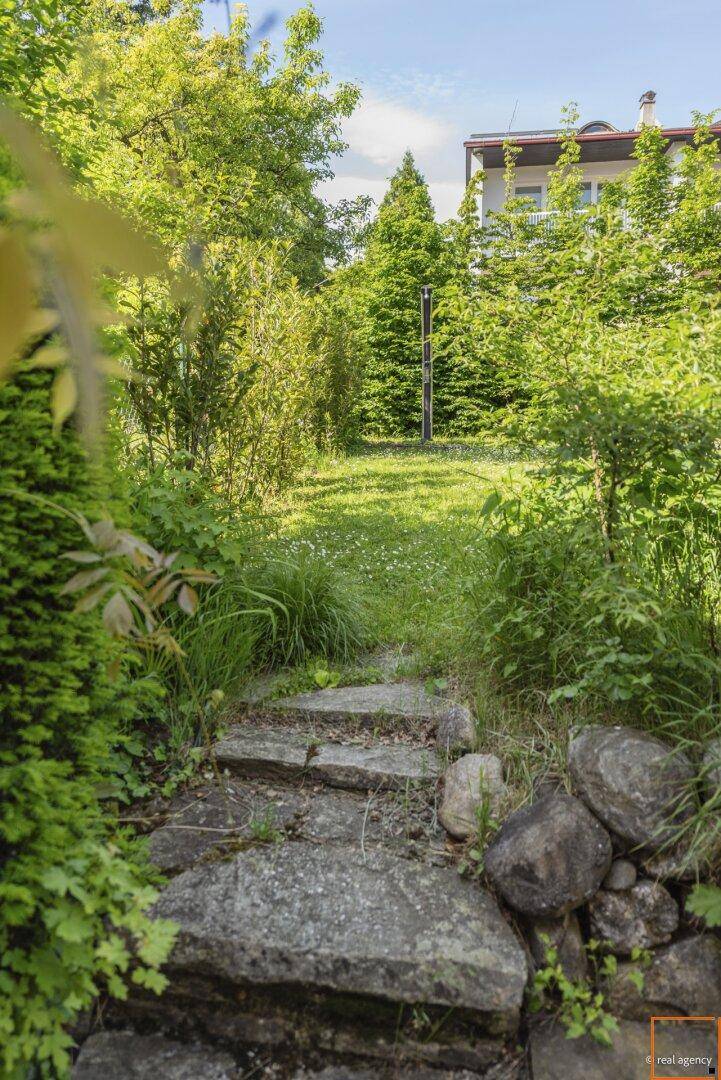 Steinpfad führt durch einen üppigen, naturbelassenen Gartenbereich mit viel Grün.