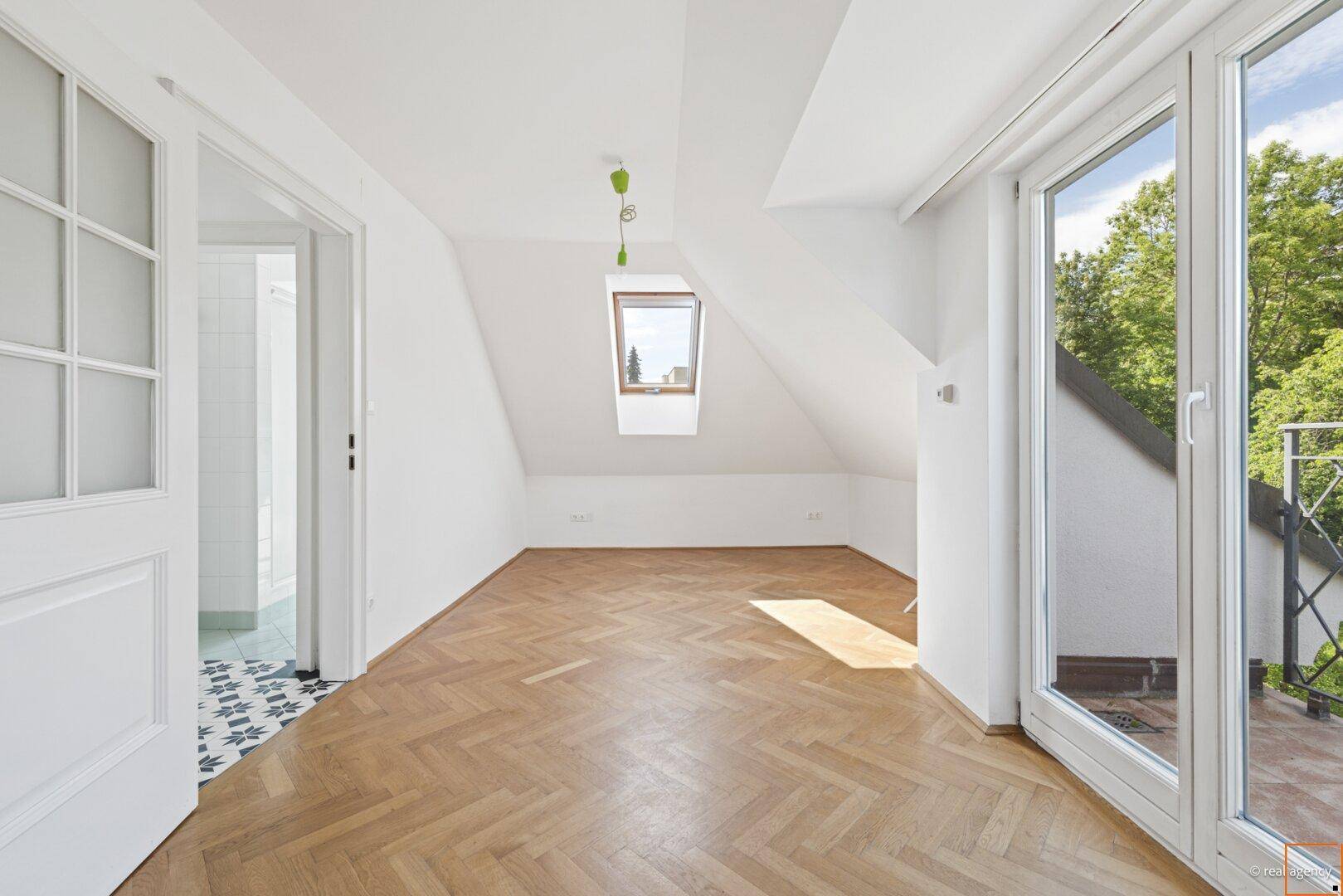 Geräumiges Zimmer mit Fischgrätparkett, Dachfenster und Zugang zu einem Badezimmer, ideal als Schlafzimmer.