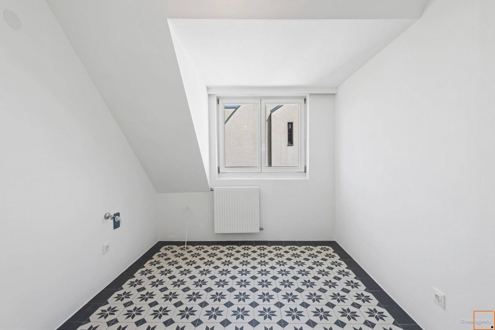 Kleiner Raum mit gemusterten Fliesen, Fenster und Anschlüssen, ideal als Hauswirtschaftsraum oder Gäste-WC.