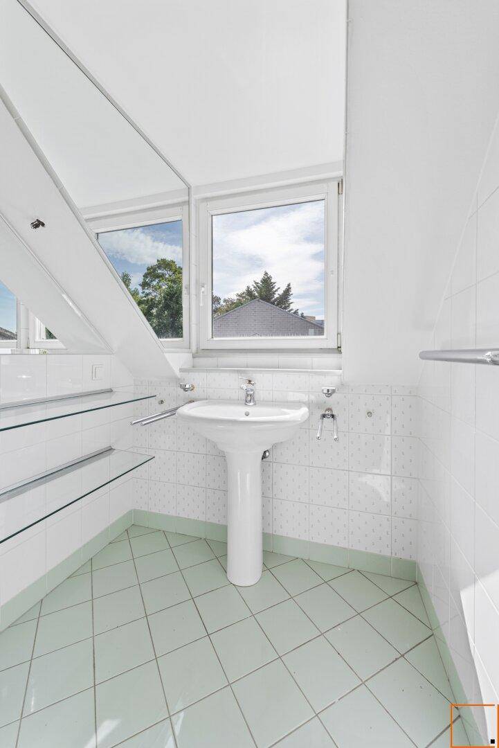 Badezimmer mit Standwaschbecken, hellen Fliesen und Fenster, das viel Tageslicht hereinlässt.