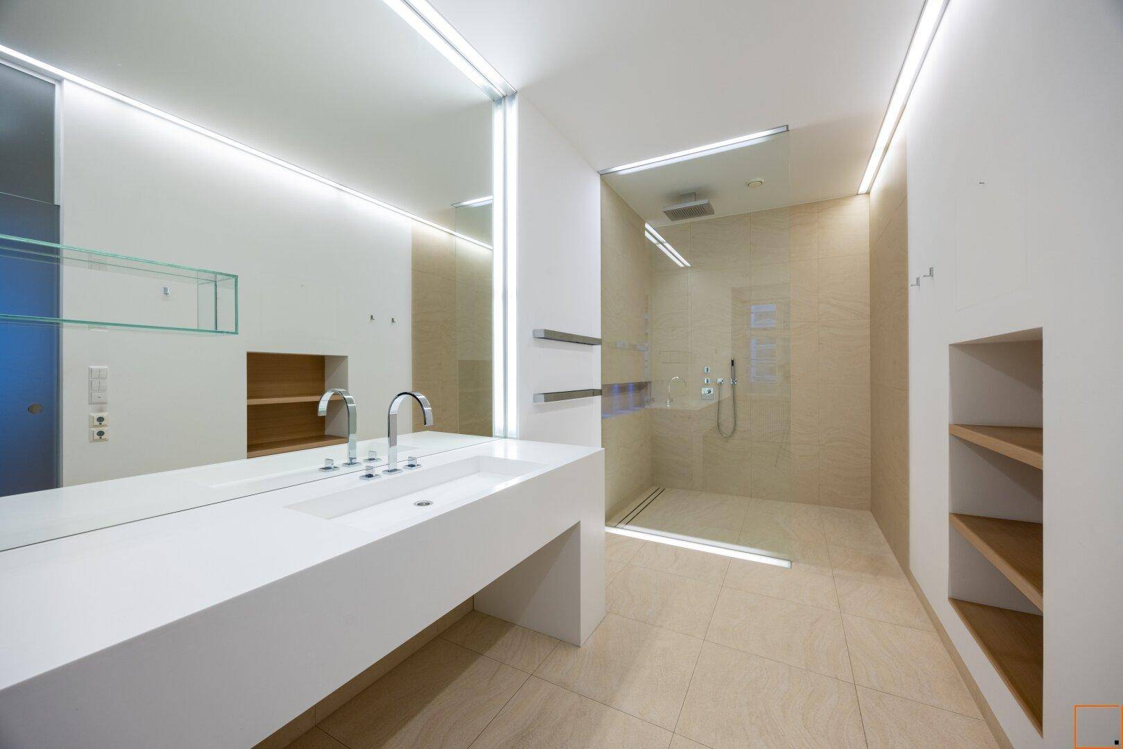 Modernes Badezimmer mit großem Waschtisch, begehbarer Dusche und indirekter Beleuchtung.