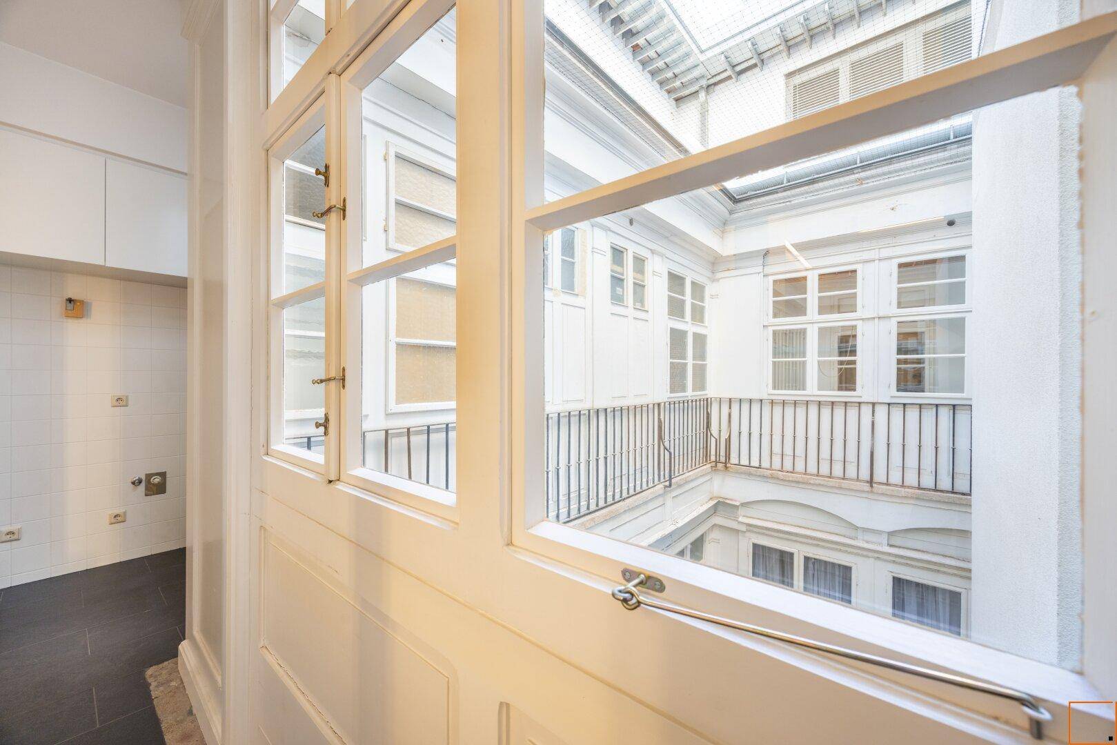 Heller Flur mit Blick auf einen Innenhof durch große Fenster, klassische Architektur.