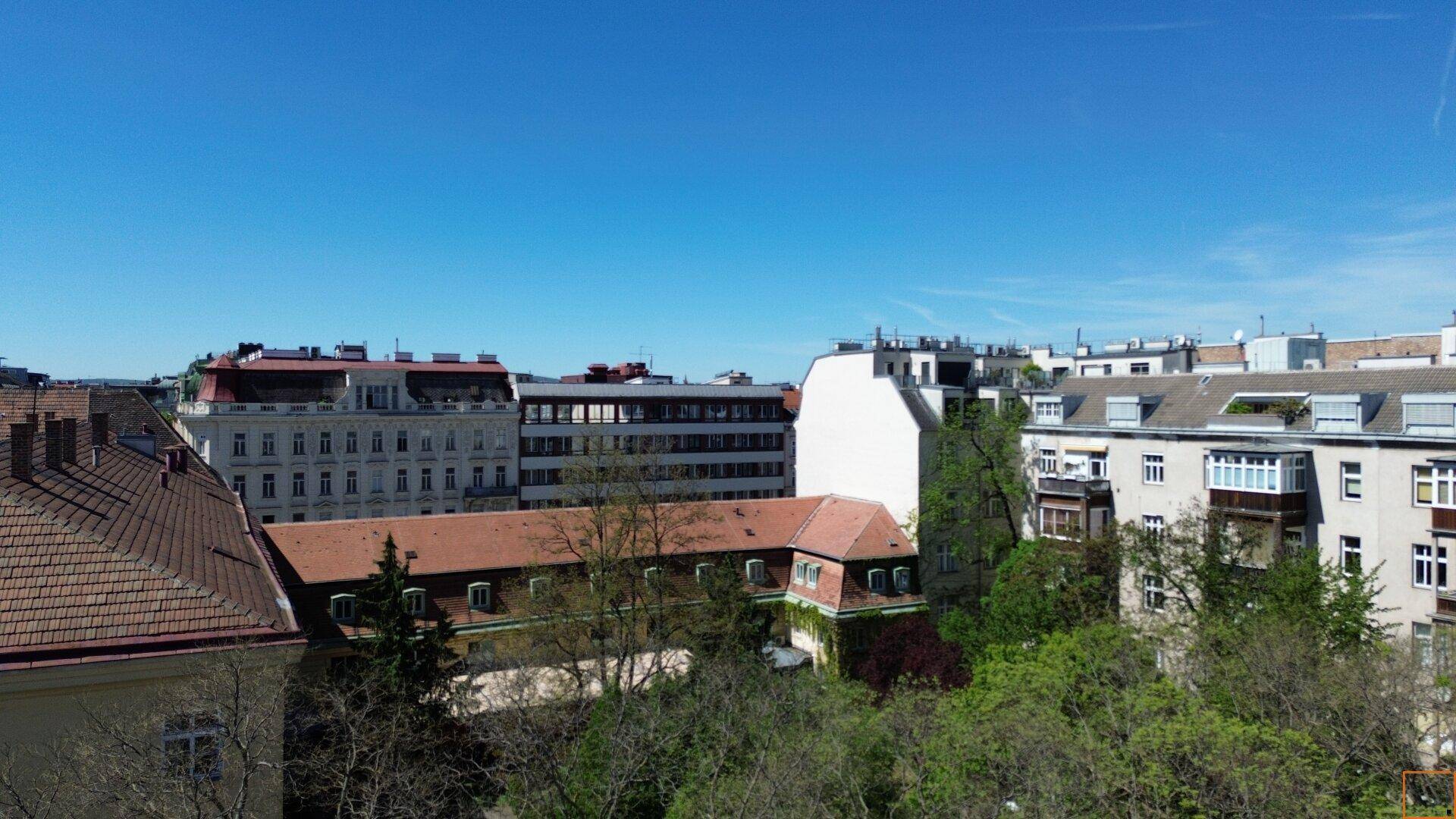 Panoramablick über städtische Dächer und Gebäude mit Bäumen unter klarem Himmel.