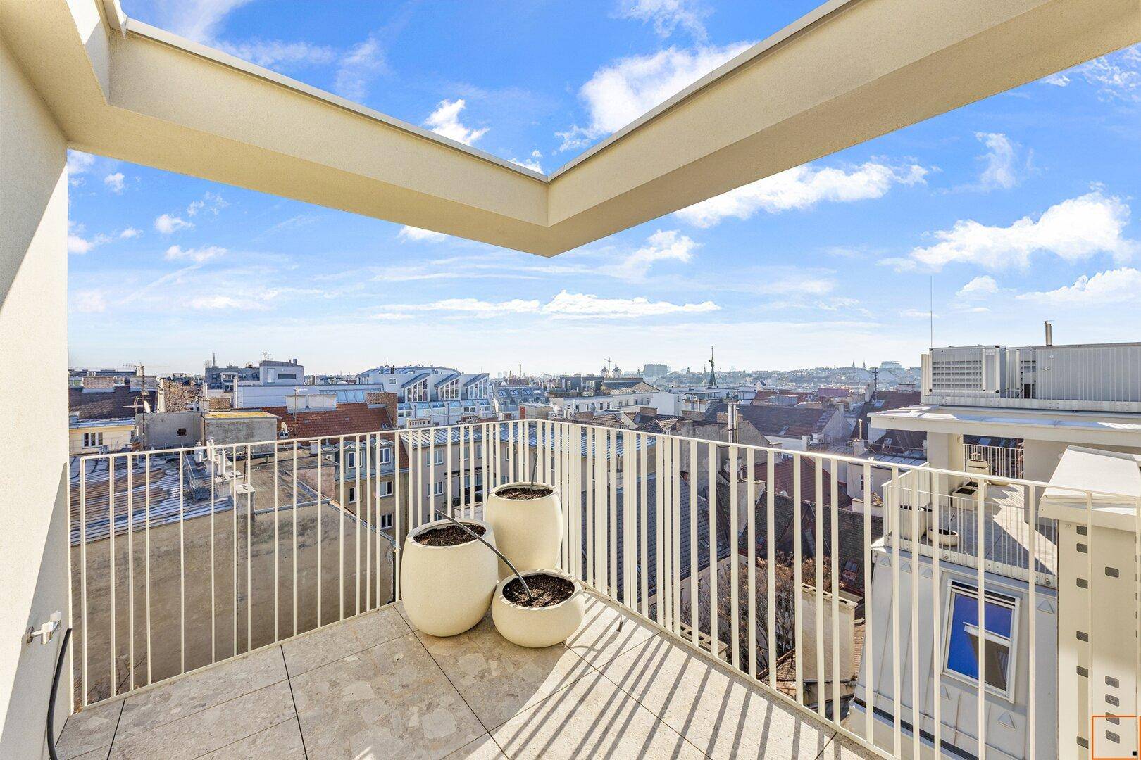 Sonnige Dachterrasse mit dekorativen Pflanzgefäßen und Panoramablick über die Stadt.